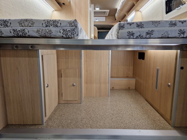 Przestrzeń magazynowa pod dwoma materacami w kamperze z drewnianymi szafkami.