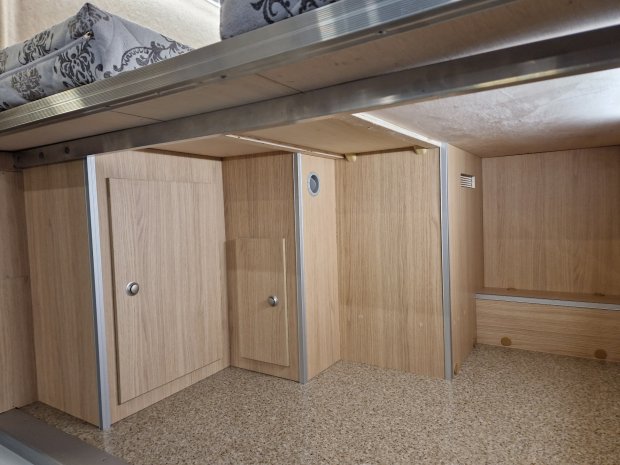 Pod łóżkiem: jasne drewniane szafki z małymi drzwiczkami