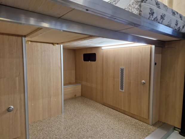 Przestrzeń pod łóżkiem z drewnianymi panelami, schowkami i lampką LED