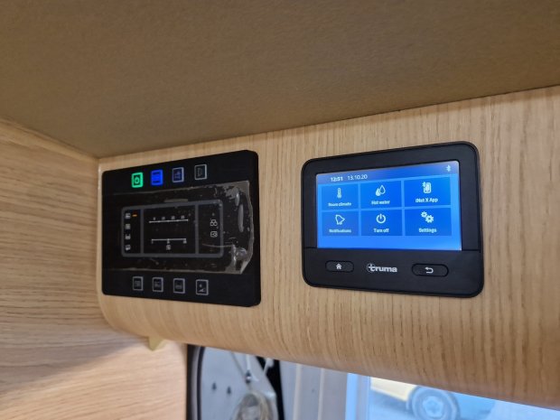 Dwa panele sterowania na drewnianej ścianie kampera: ekran Truma po prawej i panel po lewej.
