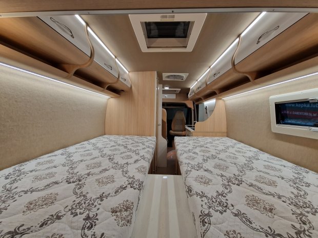 Wnętrze kampera z dwoma łóżkami, drewnianymi szafkami i oświetleniem LED