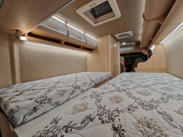 Wnętrze kampera z dwoma łóżkami, kwiatowymi materacami i drewnianymi szafkami