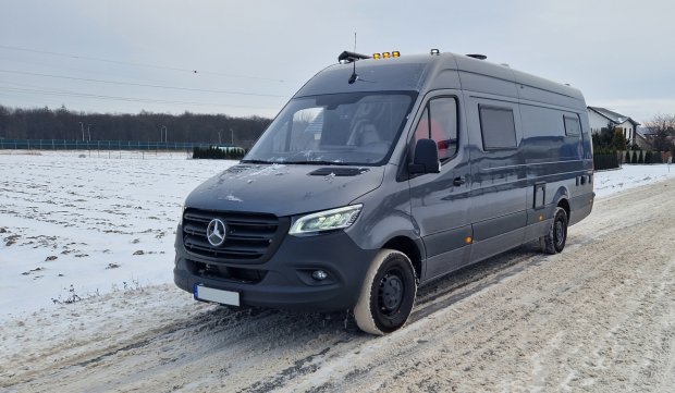 Szary kamper Mercedes Sprinter zaparkowany na śliskiej, zaśnieżonej drodze.