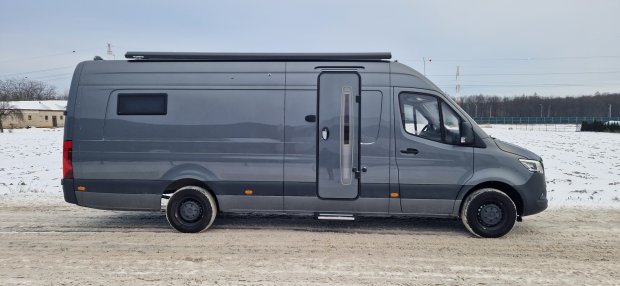 Szary kamper typu van zaparkowany na śnieżnej drodze, widok z boku