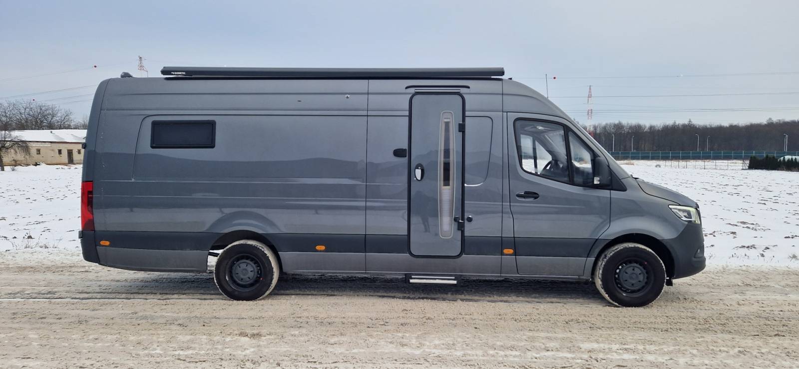 Szary kamper typu van zaparkowany na śnieżnej drodze, widok z boku