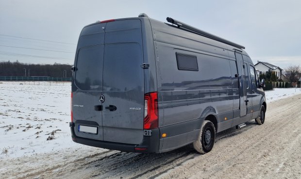 Szary Mercedes Sprinter zaparkowany na zaśnieżonej wiejskiej drodze, domy w tle