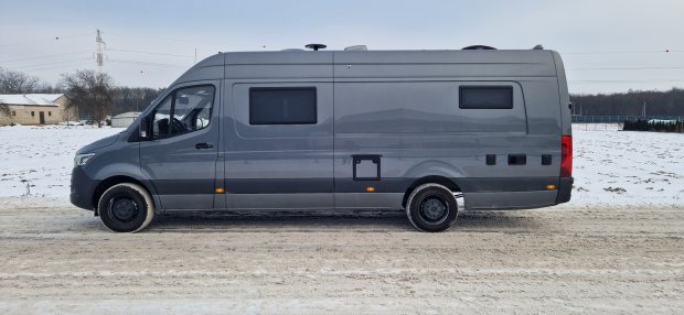 Szary kamper zaparkowany na zaśnieżonej drodze, widok z boku