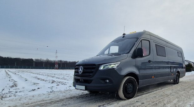 Szary Mercedes Sprinter na zaśnieżonej drodze obok pola przy pochmurnym niebie