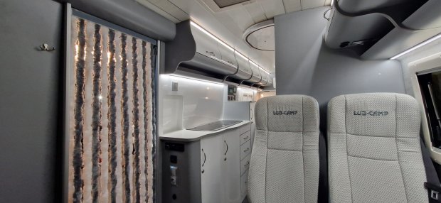 Wnętrze kampera: aneks kuchenny z szafkami i dwa tapicerowane fotele