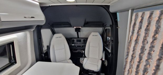 Wnętrze kampera z obrotowymi fotelami kierowcy i pasażera oraz stołem