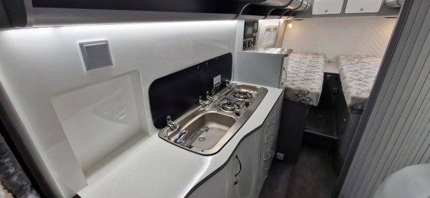 Wnętrze kampera z kompaktową kuchnią: zlewozmywak, dwupalnikowa kuchenka i łóżka