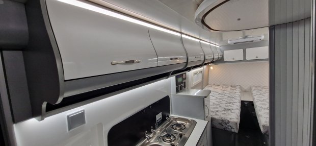 Wnętrze kampera: kuchenka, wiszące szafki i dwa rozdzielone łóżka.