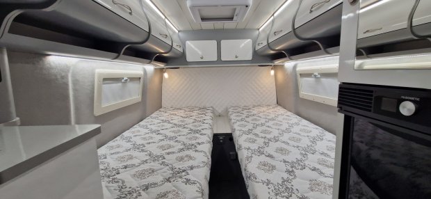 Wnętrze kampera z dwoma pojedynczymi łóżkami, szafkami górnymi i lampkami