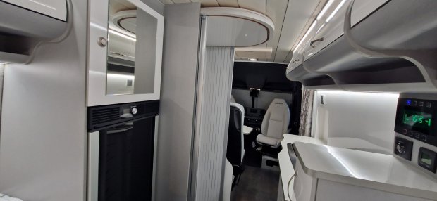 Wnętrze nowoczesnego kampera z kuchnią, szafkami i obrotowymi fotelami kierowcy.