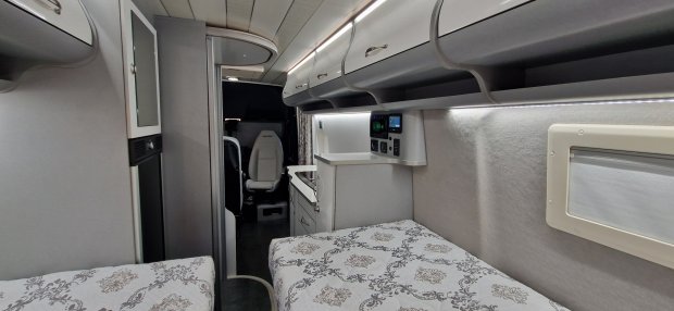 Wnętrze kampera z dwoma łóżkami, zabudowaną kuchnią i schowkami nad głową