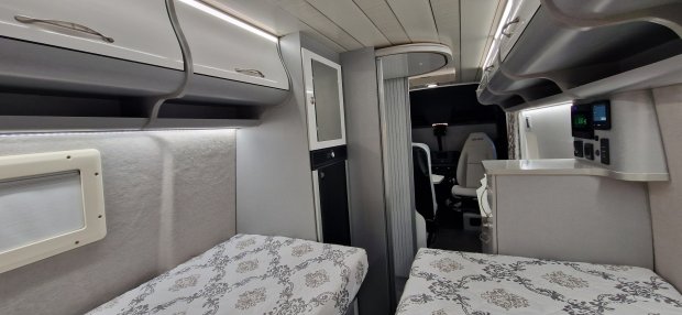Wnętrze kampera: dwa łóżka, górne szafki, aneks kuchenny i fotel kierowcy