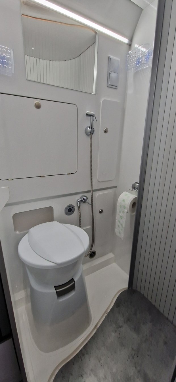 Kompaktowa biała toaleta w kamperze z prysznicem ręcznym i uchwytem na papier toaletowy