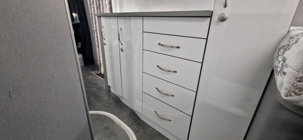 Biała lakierowana szafka z pięcioma szufladami i metalowymi uchwytami w wąskim wnętrzu