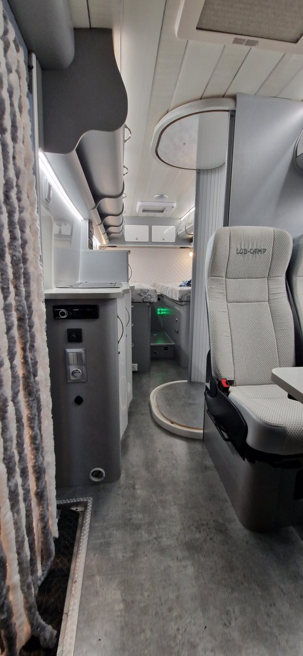 Wnętrze kampera: przejście, fotele, aneks kuchenny i łóżko z tyłu