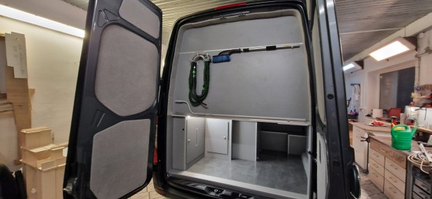 Otwarty tył furgonu z zabudową, schowkami i narzędziami w warsztacie