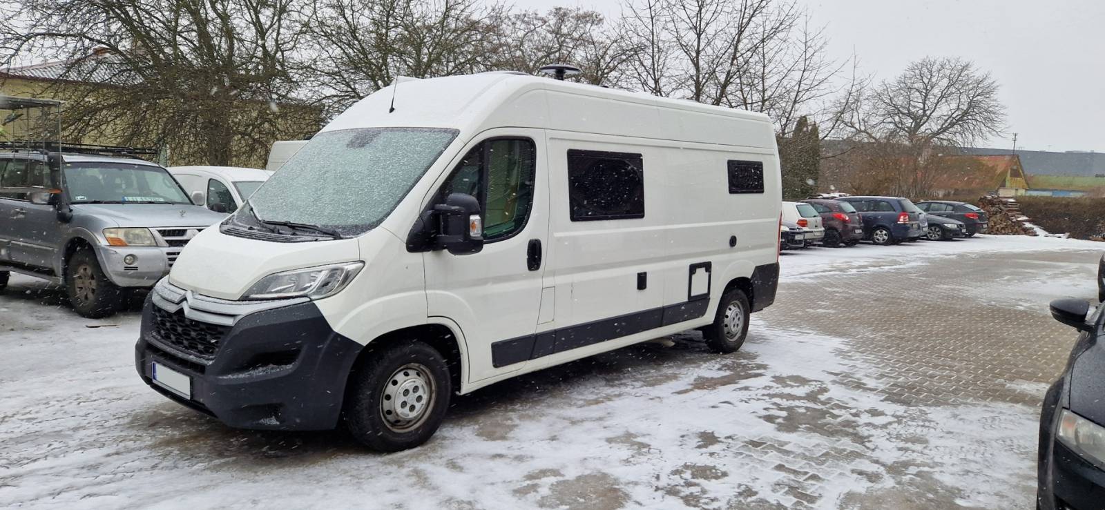Biały kamper na zaśnieżonym parkingu obok zaparkowanych samochodów