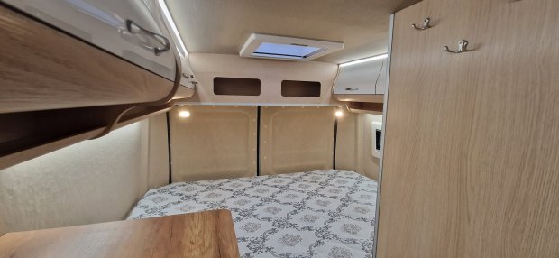 Wnętrze kampera: łóżko z wzorzystą pościelą, szafki nad głową i świetlik sufitowy