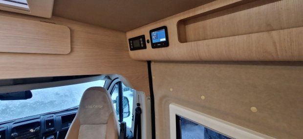 Wnętrze kampera: fotel kierowcy, drewniane szafki i panel sterowania nad kabiną