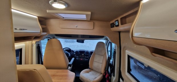 Wnętrze kampera: obrotowe fotele kierowcy i pasażera, drewniane szafki i świetlik.