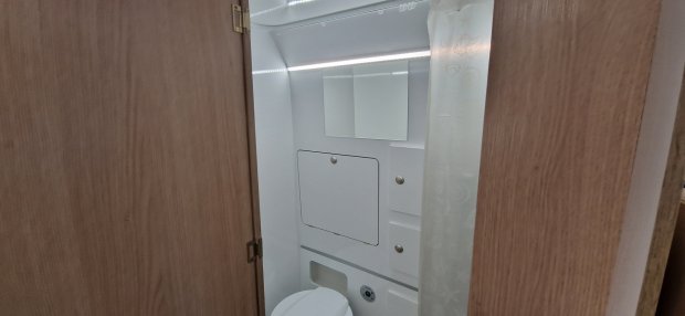 Mała łazienka w kamperze: biały sedes, lustro, szafki i zasłona prysznicowa