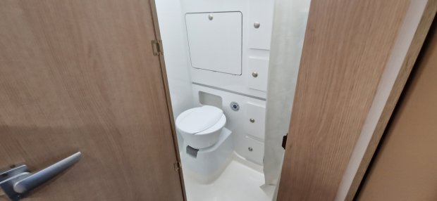 Kompaktowa biała toaleta w małej łazience kampera, częściowo otwarte drewniane drzwi
