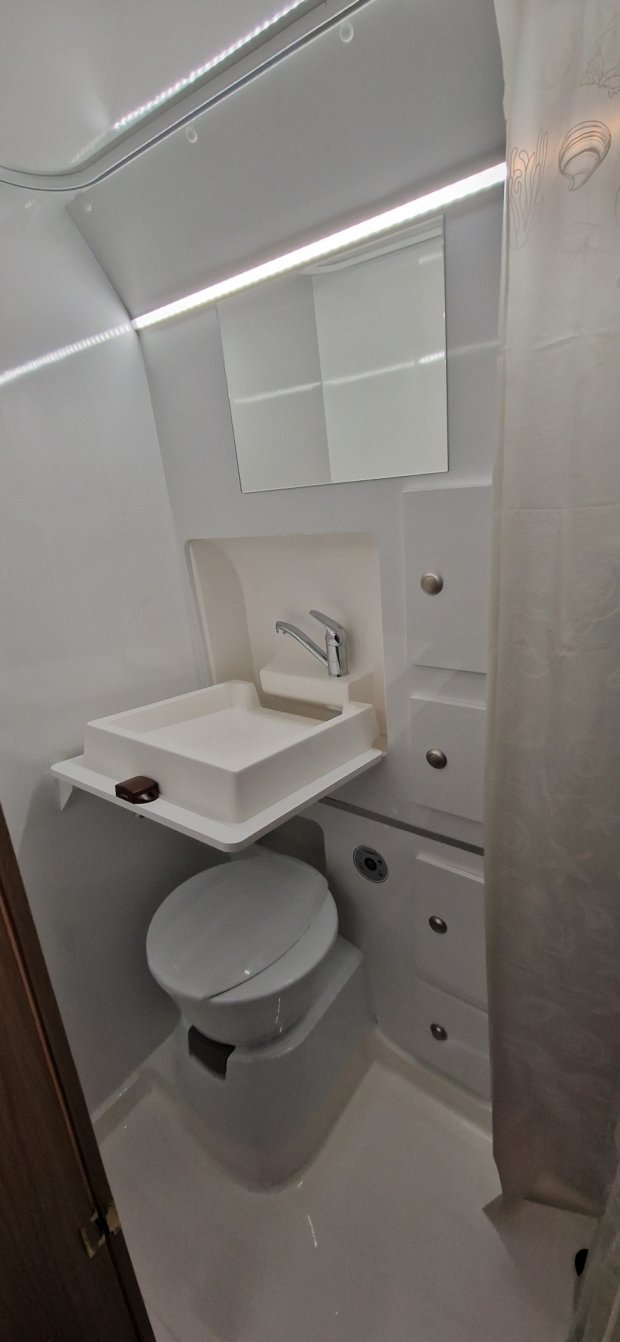 Mała biała łazienka w kamperze z umywalką, kranem, lustrem i toaletą