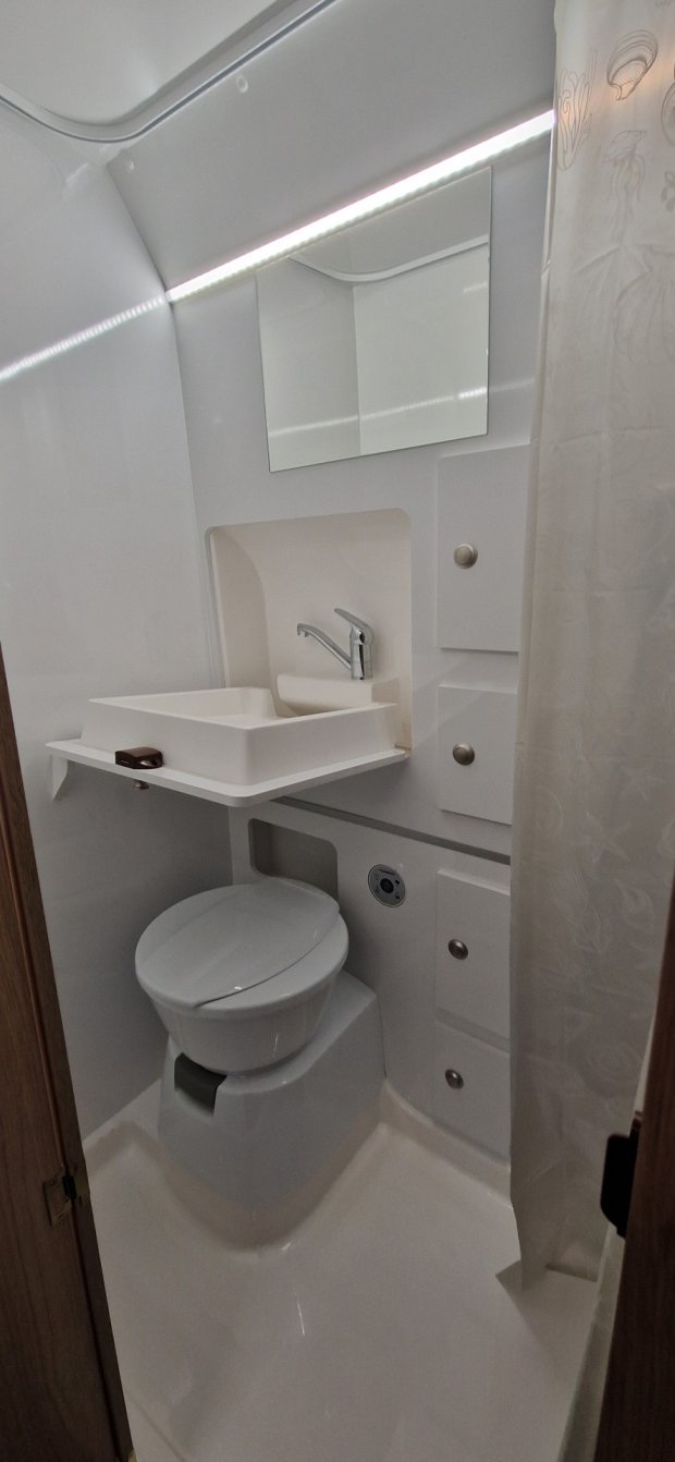 Mała biała łazienka w kamperze z umywalką, toaletą, lustrem i zasłoną prysznicową