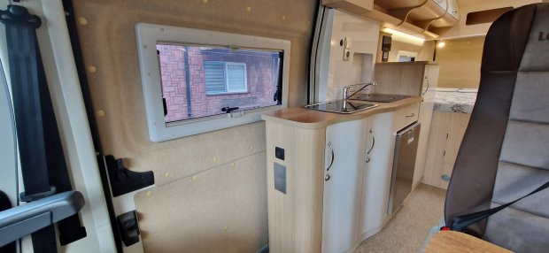 Wnętrze kampera: kompaktowa kuchnia z blatem, zlewem, szafkami i fotelem