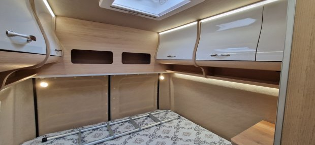 Wnętrze kampera: łóżko z drabinką i drewniano-białe szafki z oświetleniem.