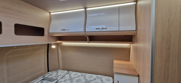 Kącik sypialny w kamperze z białymi nadstawkami, lampką i materacem