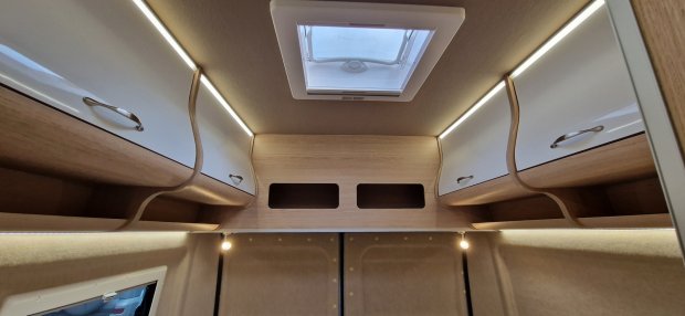 Wnętrze kampera: górne szafki, oświetlenie LED i okno dachowe nad łóżkiem