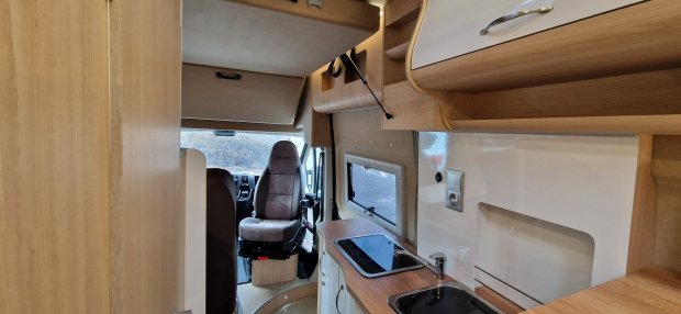 Wnętrze kampera z kuchenką i zlewem, obrotowym fotelem kierowcy i drewnianymi szafkami