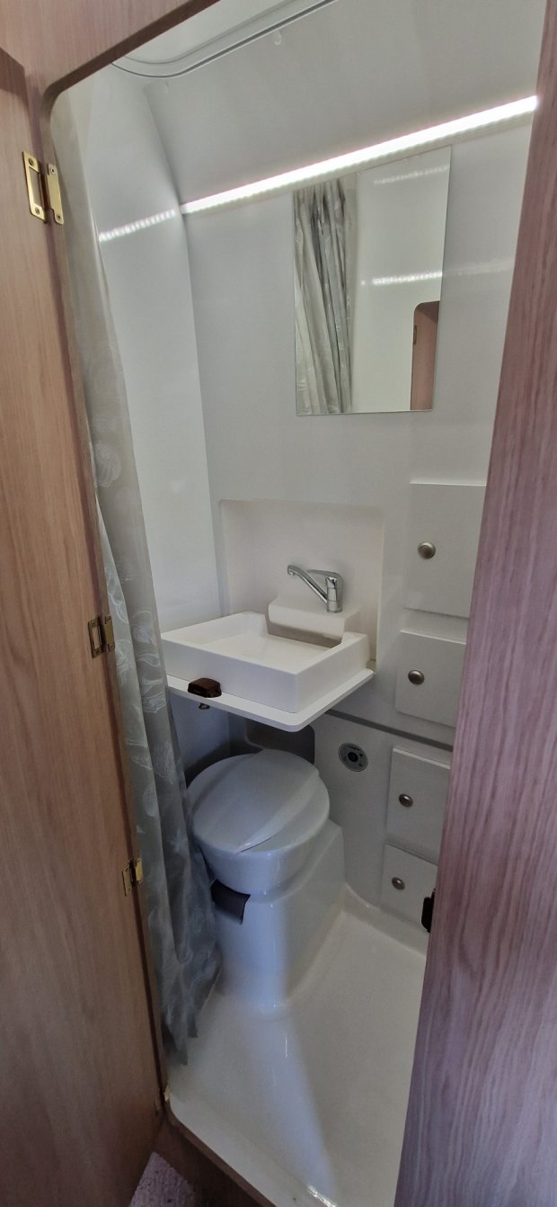 Kompaktowa łazienka w kamperze: toaleta, umywalka, lustro i zasłona prysznicowa