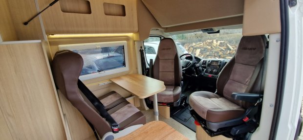 Wnętrze kampera z drewnianym stolikiem i trzema obrotowymi brązowymi fotelami.