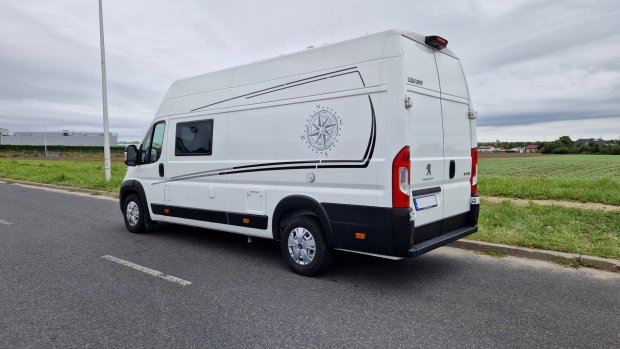 Biały kamper Peugeot z kompasem na boku zaparkowany przy polnej drodze.