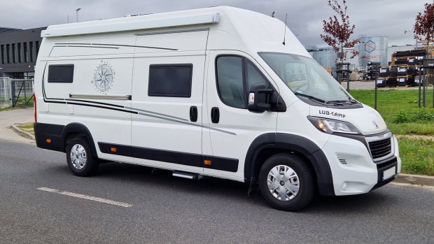 Biały kamper typu van z grafiką kompasu i czarnymi detalami zaparkowany przy ulicy