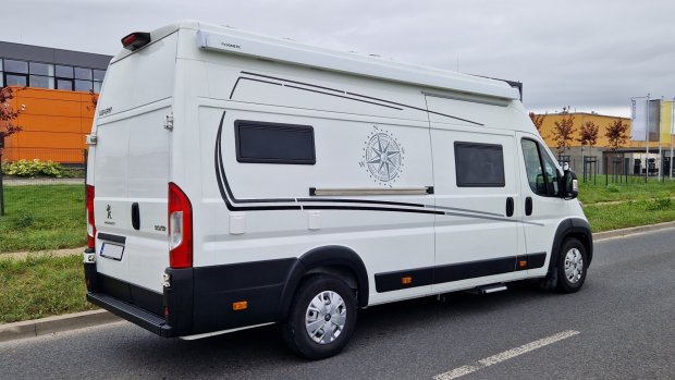 Biały kamper Peugeot z kompasem na boku zaparkowany przy chodniku