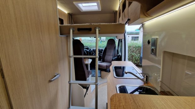 Wnętrze kampera: drabinka do łóżka, fotele kierowcy i zabudowana kuchnia z umywalką.