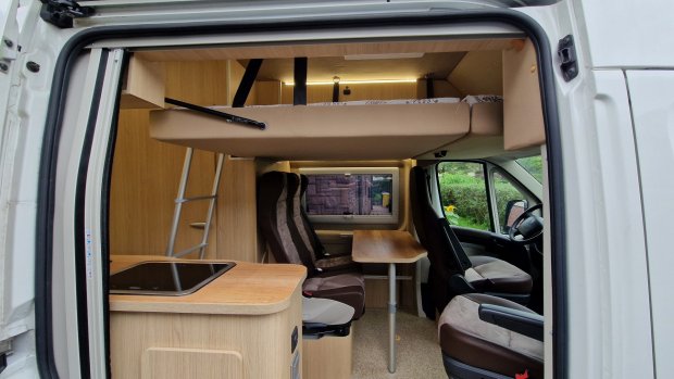 Wnętrze kampera z podwiesznym łóżkiem, stołem, siedzeniami i małą kuchnią