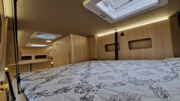 Sypialnia w kamperze z drewnianymi ściankami, oknami dachowymi i wzorzystym materacem