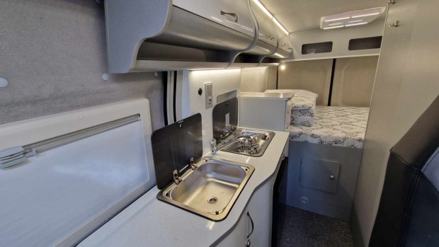 Wnętrze kampera z kuchenką, zlewem, szafkami i łóżkiem z tyłu