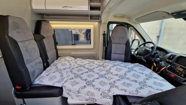 Wnętrze kampera z rozłożonym łóżkiem między fotelami kierowcy i pasażera.