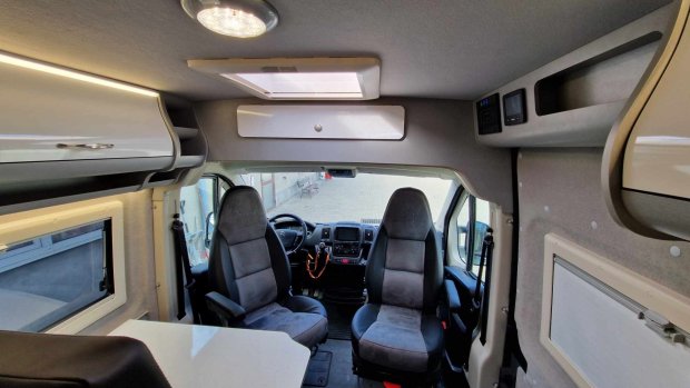 Wnętrze kampera: obrotowe fotele, kokpit, świetlik i górne szafki.