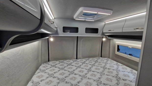 Wnętrze kampera: łóżko z wzorzystą pościelą, górne szafki, okno i świetlik dachowy