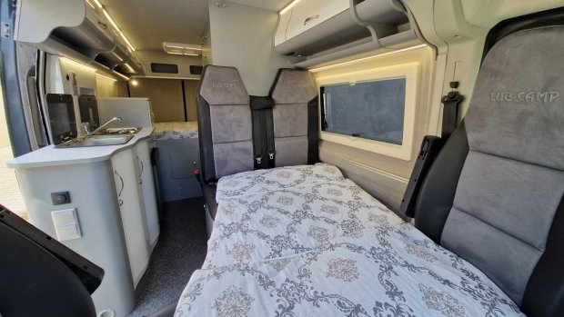 Wnętrze kampera z łóżkiem, kuchenką i szarymi tapicerowanymi siedzeniami